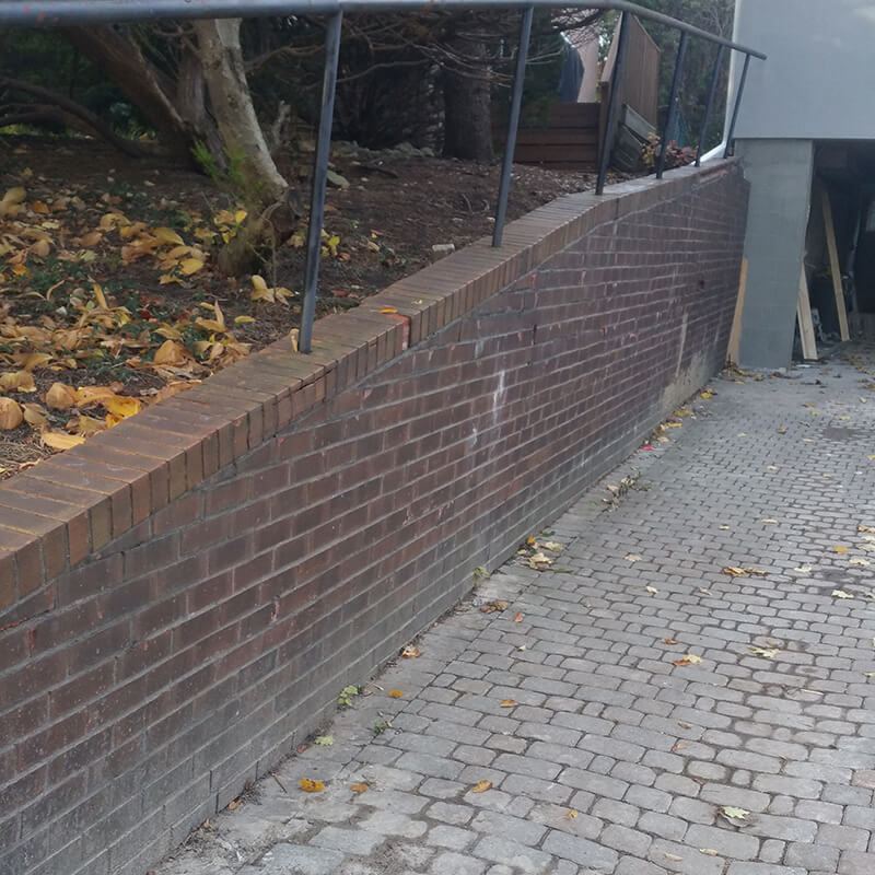 Old brick-faced retaining wall with a metal railing beside an interlock walkway