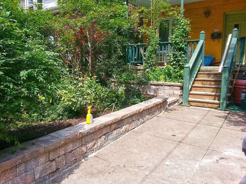 Low tan small-block wall with caps edging a concrete front patio that leads to wooden porch steps