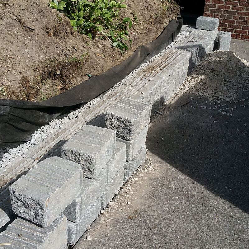 Close view of new grooved grey blocks set along the driveway, with clear stone and filter fabric behind