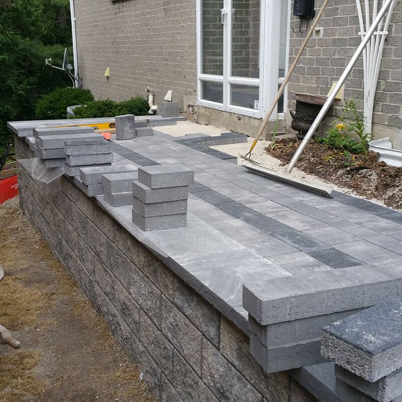 Coping set on the new wall and Artline pavers with a dark border being laid on top beside the house