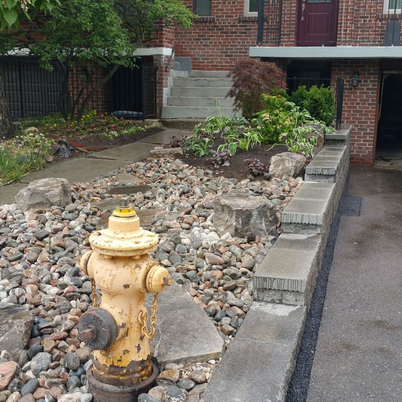 River rock and armour stone garden around a fire hydrant, with the capped block wall along the driveway
