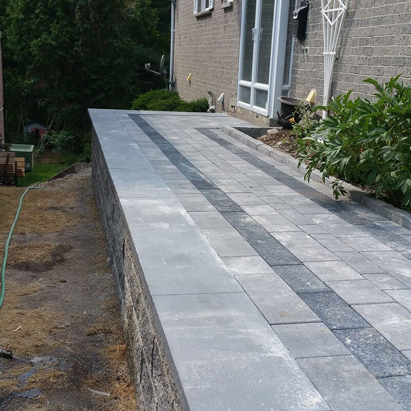 Long precast block wall with grey capstones and a paver path along the top