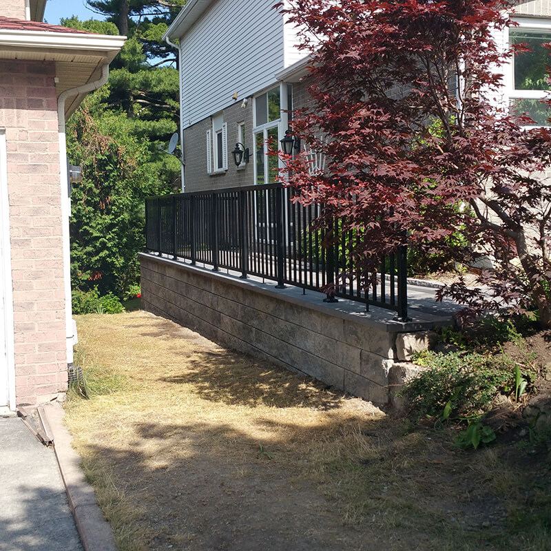 Finished precast retaining wall with a black railing and Japanese maple beside a house