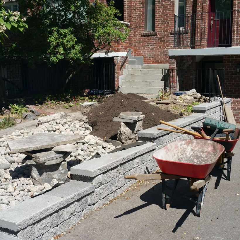 Wheelbarrow beside the capped block wall while soil and river rock are placed in the front yard