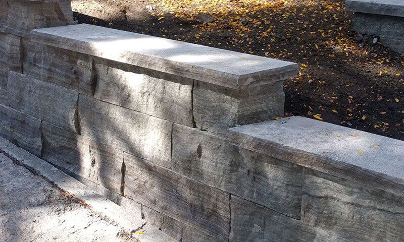 Dry-stacked Eramosa natural stone wall with a thick stone coping beside a walkway