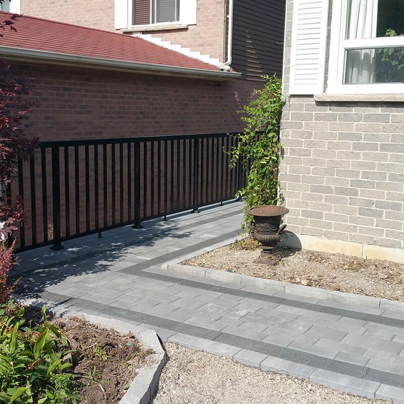 Walkway with black railing turning the corner beside the brick house