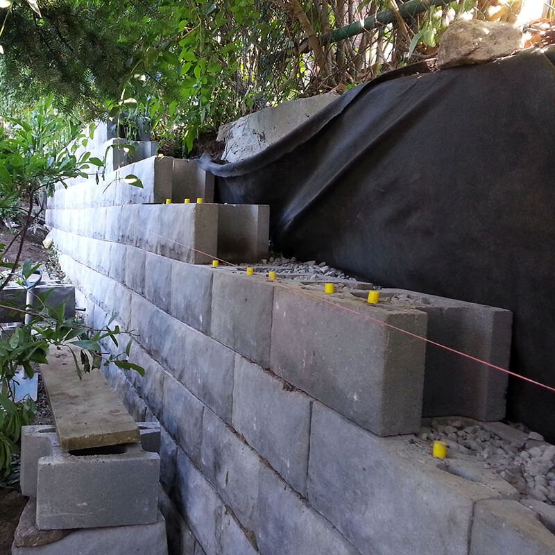 Tall precast block wall under construction with yellow fibreglass pins, a string line and filter fabric behind
