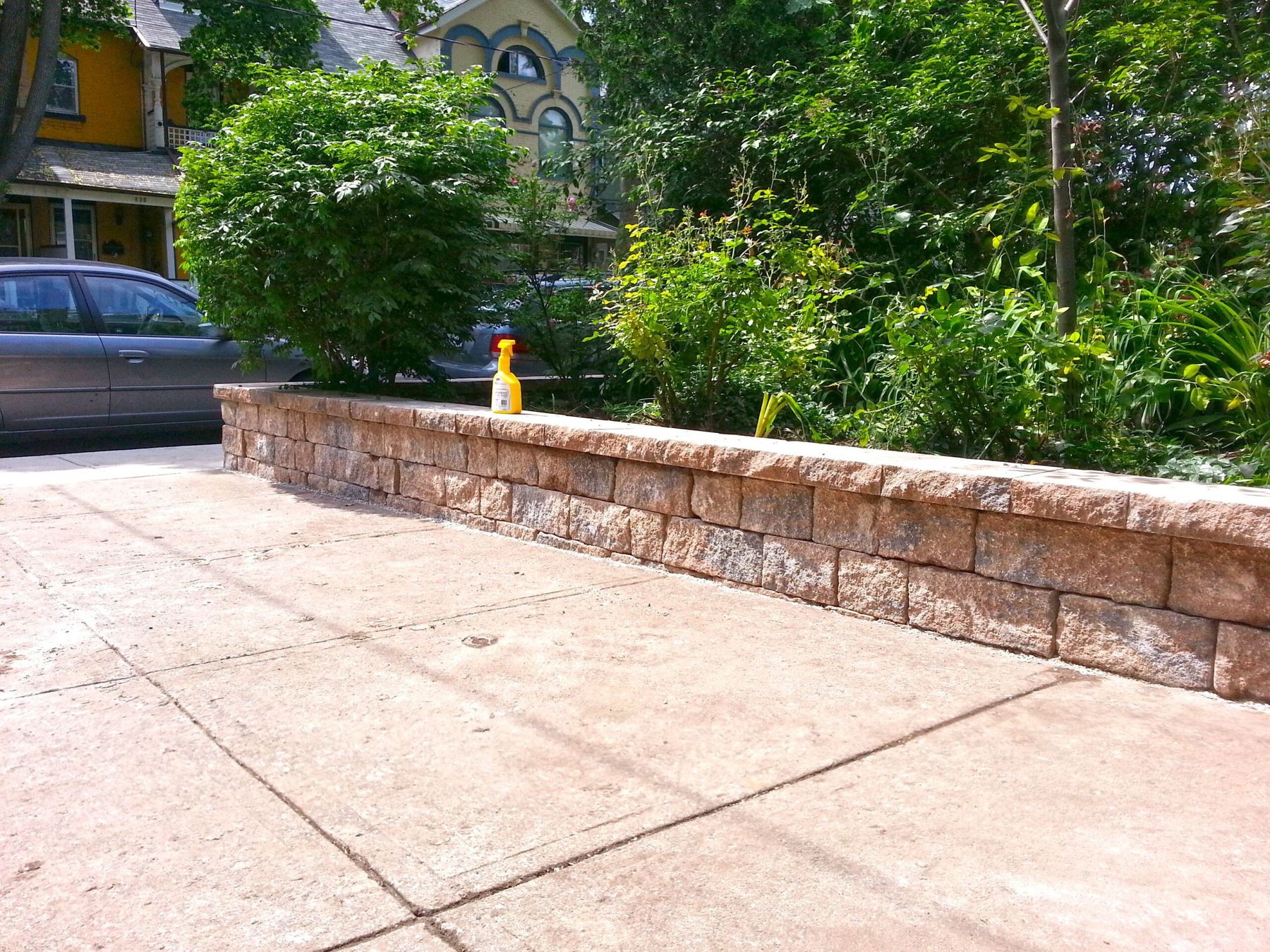 Tan precast block retaining wall with capstones holding a raised garden bed beside a concrete patio
