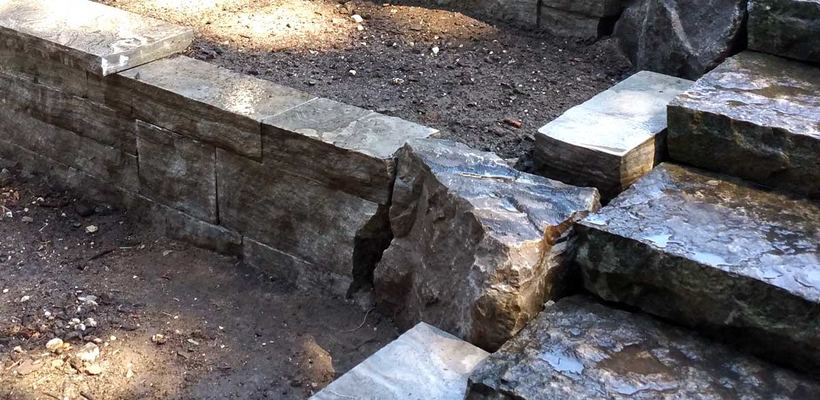 Rough armour stone steps climbing beside a dry-stacked natural stone wall with flat stone coping