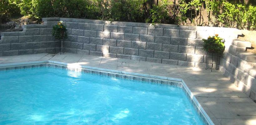 In-ground pool surrounded on two sides by tiered grey precast block retaining walls with planters on the coping