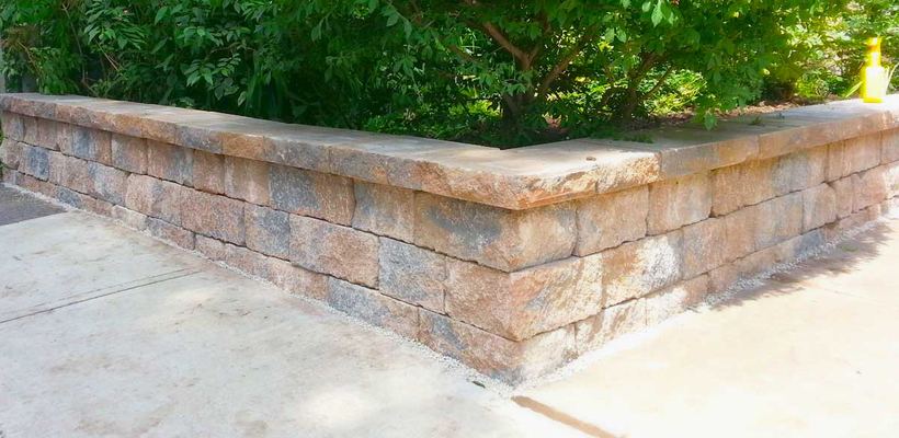 Tan small block corner wall with shrubs planted behind it